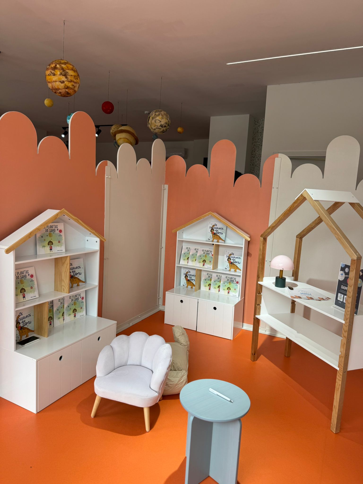 Zona da livraria com estantes em forma de casinha, livros do Samu e planetas suspensos no tecto.